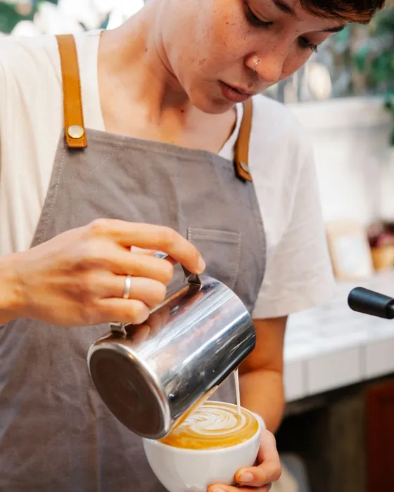 A barista pouring steamed milk into a cup